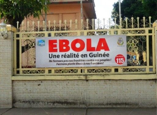A poster hanging on a fence saying "Ebola: Une rÃ©alitÃ© en GuinÃ©e"