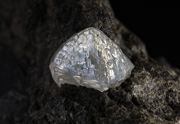 A clear, faceted diamond on a black rock