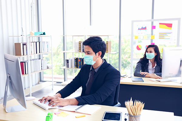 two office workers at computers wearing masks for Covid-19 protection