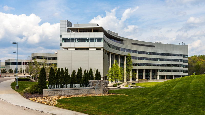 A tan curved building with a sign stating "Spallation Neutron Source" and "Oak Ridge National Laboratory."