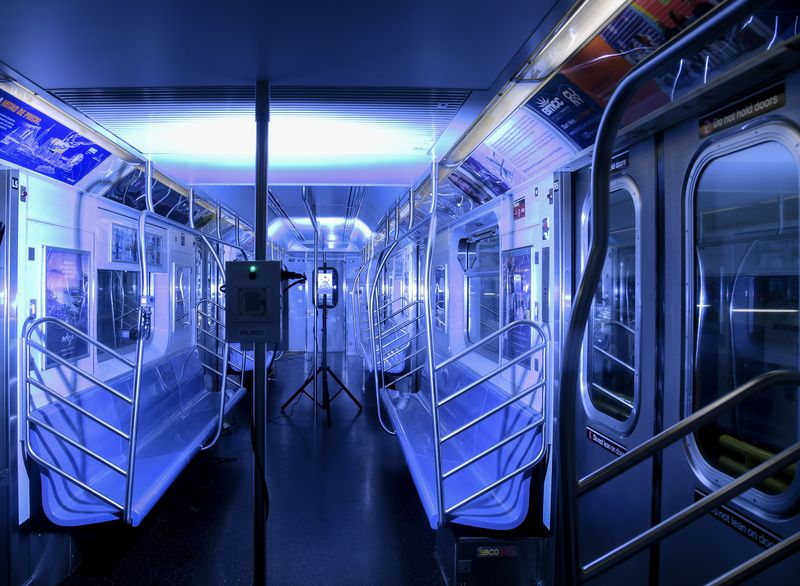 inside of a subway car with seats at left and right, all bathed in a blue light