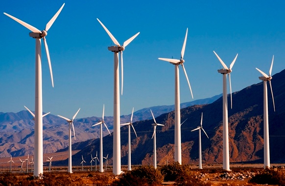 A group of wind turbines; brown mountains and blue sky are in the background
