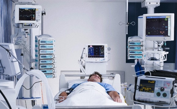 Full-length view (photo) of a male patient in a hospital bed, with many medical devices surrounding him