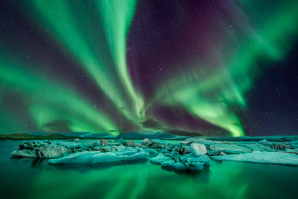 green ribbons of light in the night sky over a frozen landscape with water in the foreground