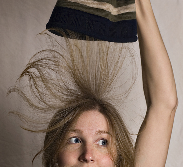 young girl with blond hair taking off a knit cap and her hair is standing on end