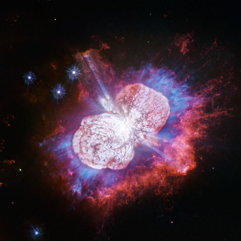 Image of Eta Carinae, which looks like two lobes of expanding gas clouds in light colors, surrounded by blue, purple, and red hues of radiating gases
