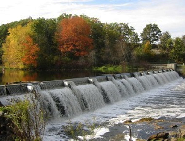 water flowing over a dam with trees in the background